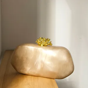 Detailsicht marmorierte Hartschalen Abendtasche in Champagner mit goldenem Korallenverschluss.