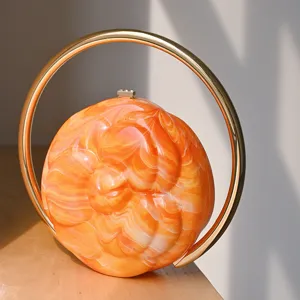 Camellia embossed orange marble acrylic clutch bag with golden round handle detail.