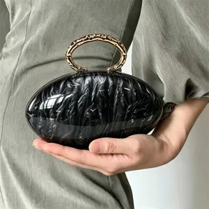 Elegante bolso clutch ovalado efecto marmol negro blanco con asa de anillo metal dorado.