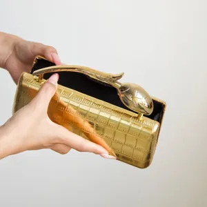 Detailaufnahme einer goldenen Metallic-Clutch mit Kroko-Prägung und edlem Tulpen-Metallgriff.