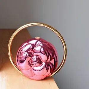 Close-up view of the exquisite pink camellia embossed round handbag with large gold handle.