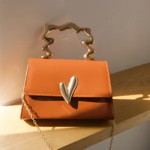 Caramel trendy small square bag detail showing irregular metallic handle and heart clasp.