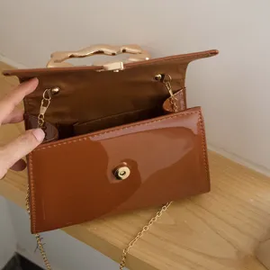 Brown patent leather shoulder bag with irregular gold handle and chain strap for women.