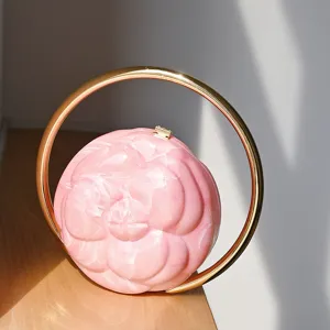 Pink camellia embossed round acrylic clutch handbag with a stylish gilded circular metal handle.