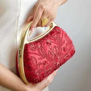 Dettaglio di ricamo floreale di perle su pochette da sera rossa con manico in metallo.