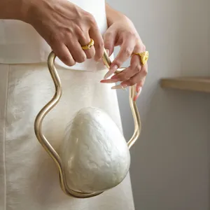 Close-up detail of the unique pearlescent eggshell evening bag with gold wavy handle in use.