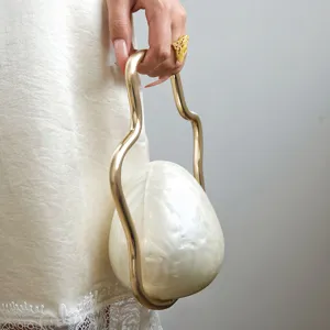 Close up detail of unique pearlescent eggshell evening bag featuring curved gold metal handle.