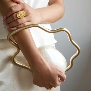 Detailed view of a unique irregular evening clutch with metallic gold handle and pearlescent finish.