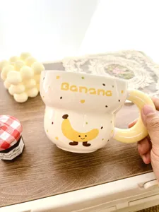 Detailed close-up shot of a cute ceramic banana mug with cartoon pattern and yellow handle.