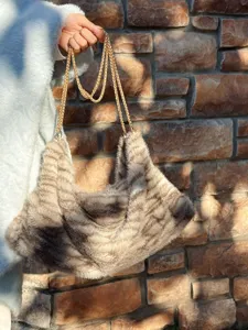 Gedetailleerd overzicht van de pluizige nepbont tas met gouden ketting tegen stenen muur.