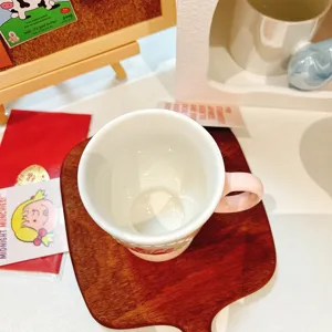 Detail view of elegant ceramic coffee mug with pink handle and floral pattern resting on wood coaster.