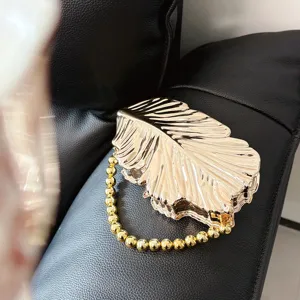 Goldene metallische Blatt-Clutch Detailansicht, glänzendes Finish mit elegantem Perlengriff für Partys.