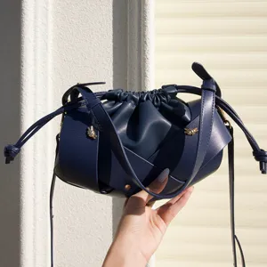 Close-up of dark blue leather drawstring crossbody bag featuring chic cross straps and soft pleats.