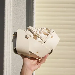 Detail shot of white leather bucket bag with crossover strap design and drawstring closure.