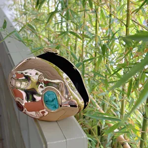 Close-up detail of metallic abstract evening clutch bag with irregular curves and gemstone decor.