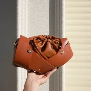 Detailed shot of brown leather drawstring crossbody bag with unique cross strap and pleats.