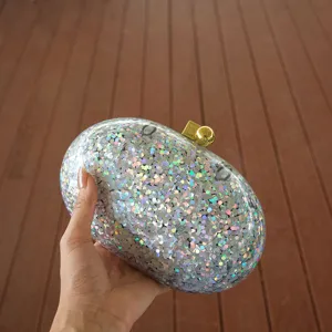 Detail view of sparkly holographic acrylic clutch bag featuring golden ball clasp.