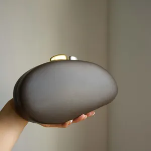 Detail shot of a minimalist matte brown oval shell acrylic clutch bag for evening events.