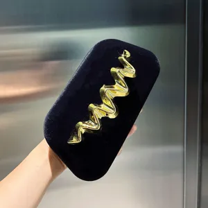 Detail shot of elegant black velvet clutch bag with a luxury gold metallic wave decoration.