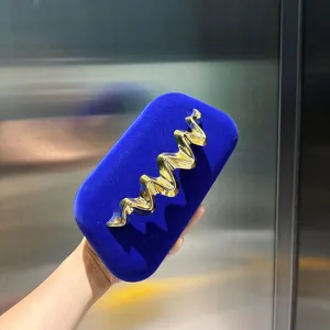 Detail shot of blue velvet box clutch bag featuring striking gold wave metal design accent.