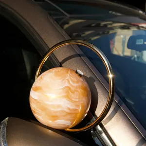 Nahaufnahme der runden Marmor Acryl Abendtasche mit goldenem Ringgriff im Sonnenlicht.
