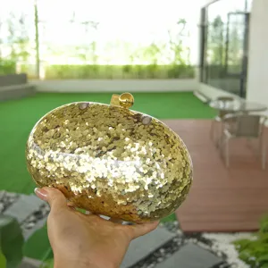 Detailed view of the elegant gold glitter acrylic oval evening clutch bag handheld in outdoor setting