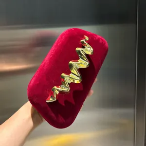 Red velvet box clutch bag with elegant golden metal wave detail, luxury fashion design.