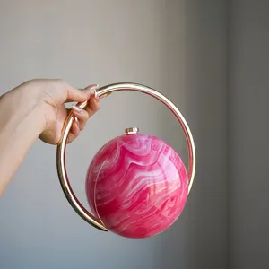 Detailansicht einer stilvollen runden Abendtasche mit rosa Marmormuster und goldenem Ringgriff.