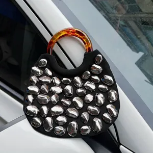 Detailed closeup of the stylish black handbag featuring metallic stone studs and tortoiseshell handle.