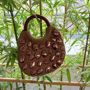 Brown canvas handbag detail featuring dark round handle and glossy irregular stone decorations.