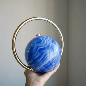 Stilvolle kugelförmige Abendtasche mit blauem Marmormuster und vergoldetem Ringgriff.