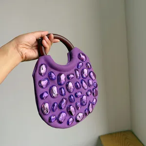 Purple fabric handbag detail featuring unique glossy metallic studs and wooden ring handle.