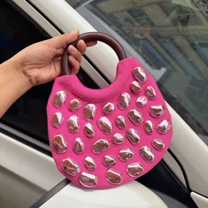 Pink canvas handbag with circular dark handle and unique metallic irregular stones.