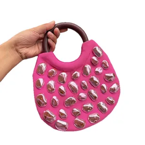 Pink canvas handbag with round wooden handle and metallic stone studs for women fashion.