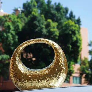 Close-up of the sparkling gold crescent handbag showing the glittering sequin texture outdoors.