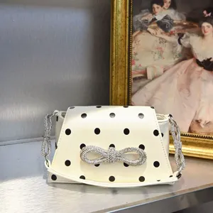 Detailaufnahme einer weißen Pünktchen-Schultertasche mit funkelnder Strass-Schleife und Kette.