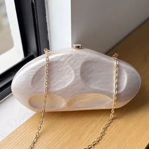 Detail view of the elegant irregular acrylic evening clutch bag with glossy finish and gold chain.