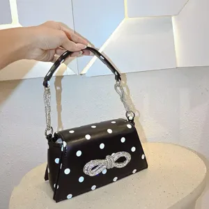 Schwarze Umhängetasche mit weißen Punkten, Strass-Schleife und glitzerndem Kettengriff.