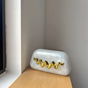 Detailansicht der weißen Acryl Abendtasche mit Marmormuster und edlem goldenen Wellen-Dekor.