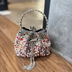 Elegante bolso tipo cubo de perlas y estrás con asa de anillo metálico y borlas.