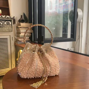 Vista detallada del elegante bolso saco de perlas con asa redonda dorada y borla colgante.