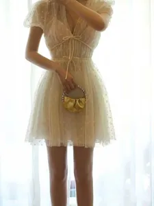 Detail shot of shiny gold metallic ruched mini handbag with crystal handle and sheer mesh dress.