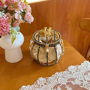 Detailed shot of metallic cage bucket bag with black rhinestones, pearl pendant and satin pouch.