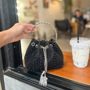 Vista detallada del elegante bolso tipo cubo negro de cuentas con asa de metal y borlas.