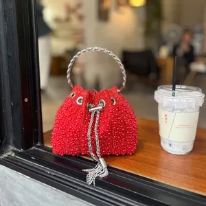 Detalle del bolso tipo saco de cuentas rojas con pedrería brillante y asa de cadena metálica.