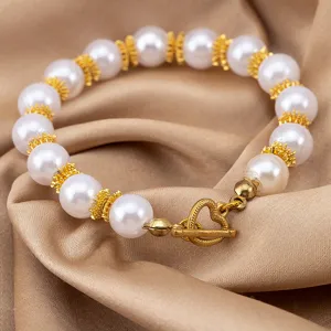 Close-up detail of white pearl bracelet with gold spacers and heart OT clasp design.