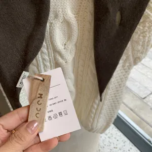 Close-up detail of knitted triangular scarf showing soft cable knit texture and branded tag.