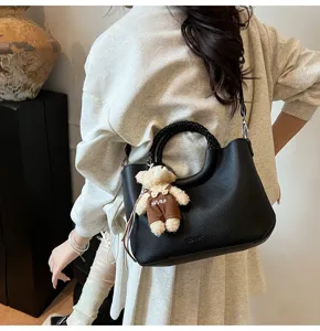 Modische schwarze Leder-Eimer-Umhängetasche mit geflochtenem Griff und süßem Bärenanhänger.