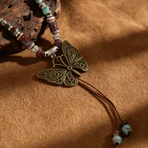 Λεπτομερής εικόνα boho vintage κεραμικού κολιέ με χάντρες και μεγάλο χάλκινο μενταγιόν πεταλούδα.