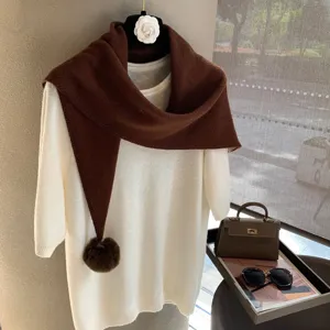 Detailed view of the brown knitted triangular scarf with pom-pom and white knit top set.